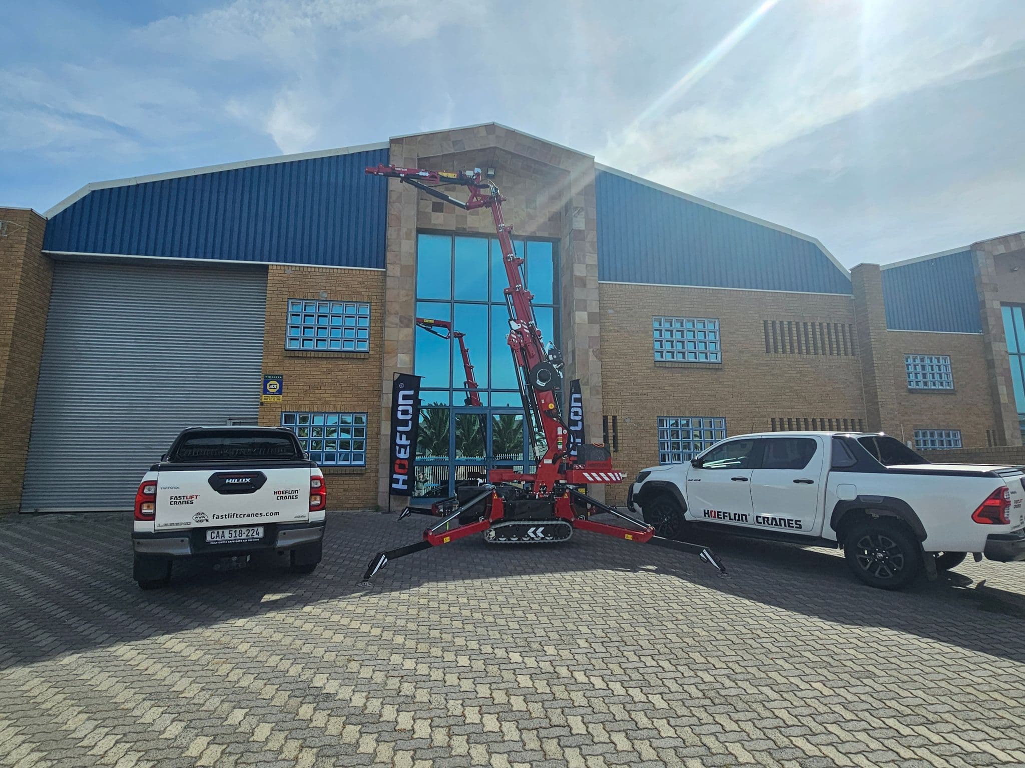 Hoeflon kraan buiten voor een gebouw met twee voertuigen van Fastlift Cranes.