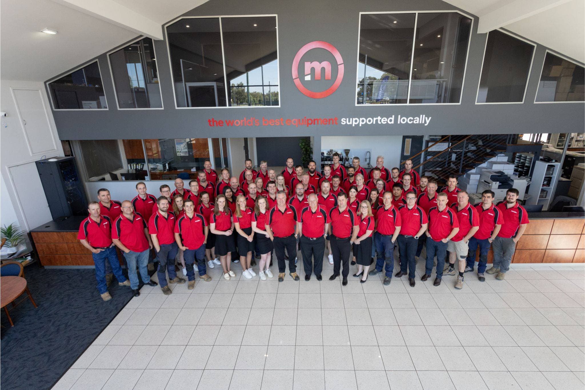 Groepsfoto van het Monitor-team in rode shirts in een kantoorruimte.