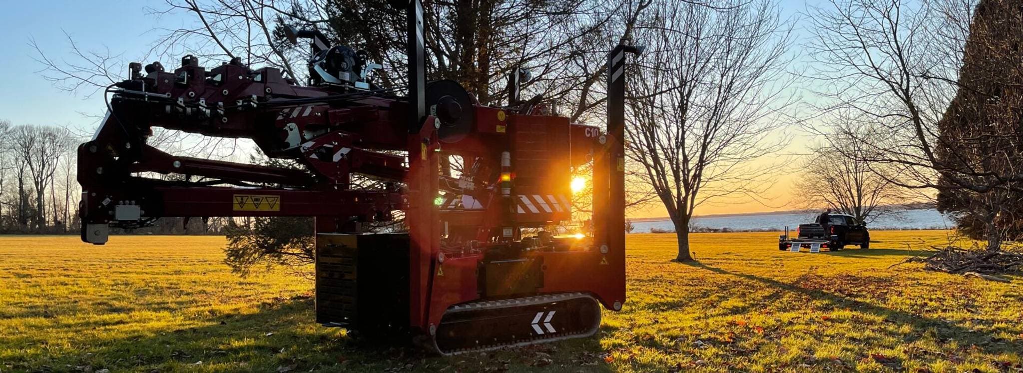 Hoeflon kraan in de zon, met een truck op de achtergrond en bomen rondom.
