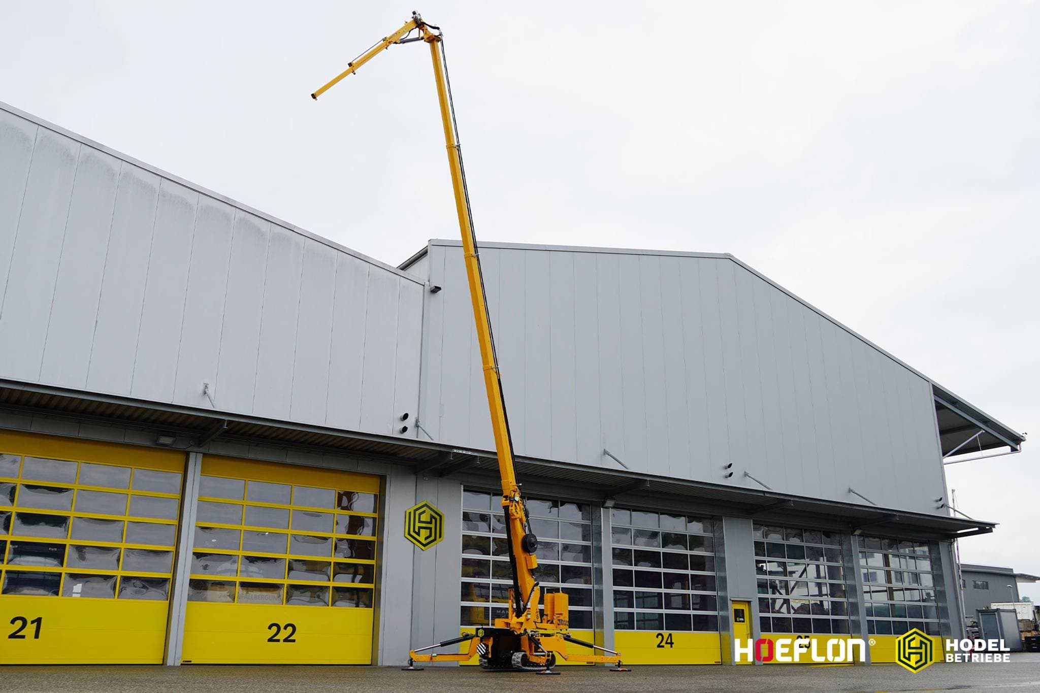 Hoeflon C10e rupsvoertuigkraan met hoge hijsarm voor een gebouw.